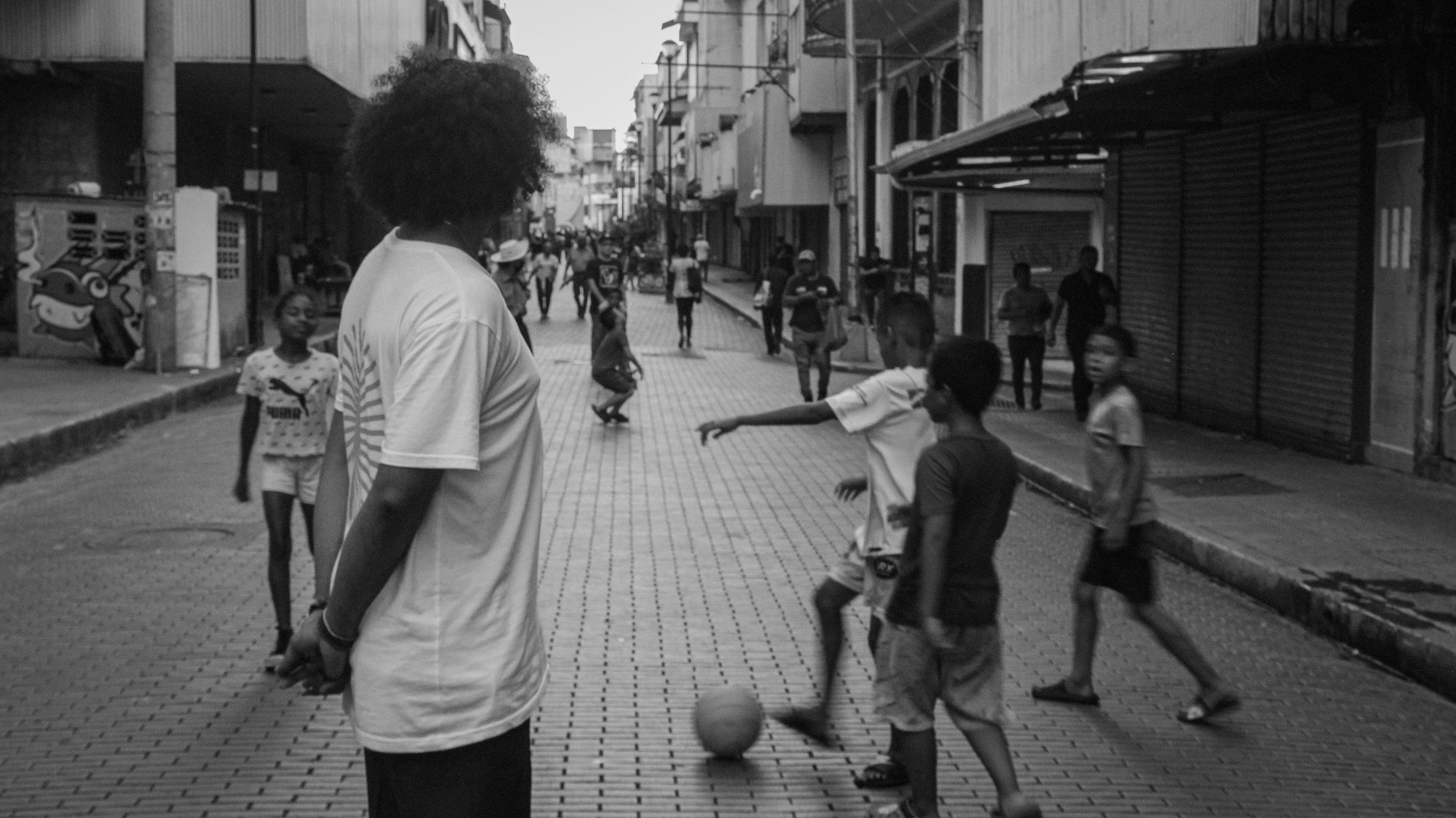 A black and white street scenery of kids playing football in the streets